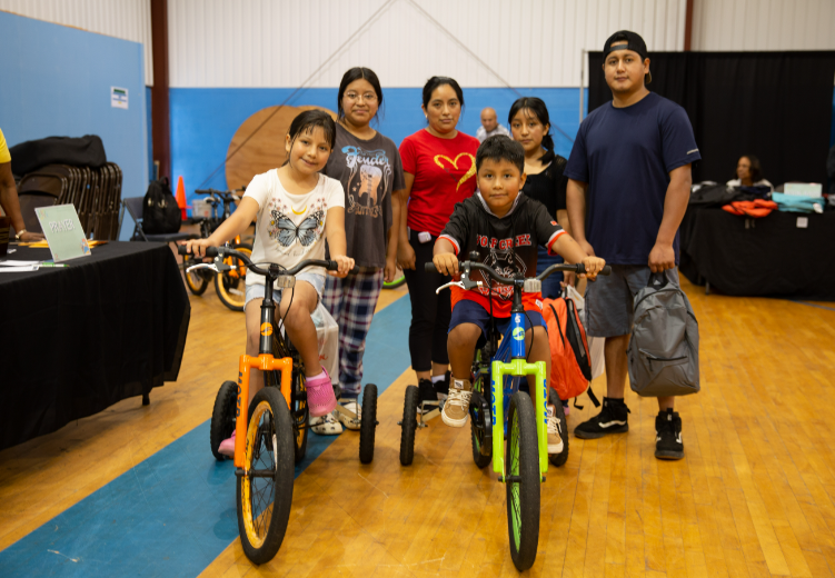 Family with two children on bicycles posing at a community event in a gymnasium.