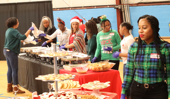 Volunteers serving food at a holiday event with tables of desserts and festive attire.